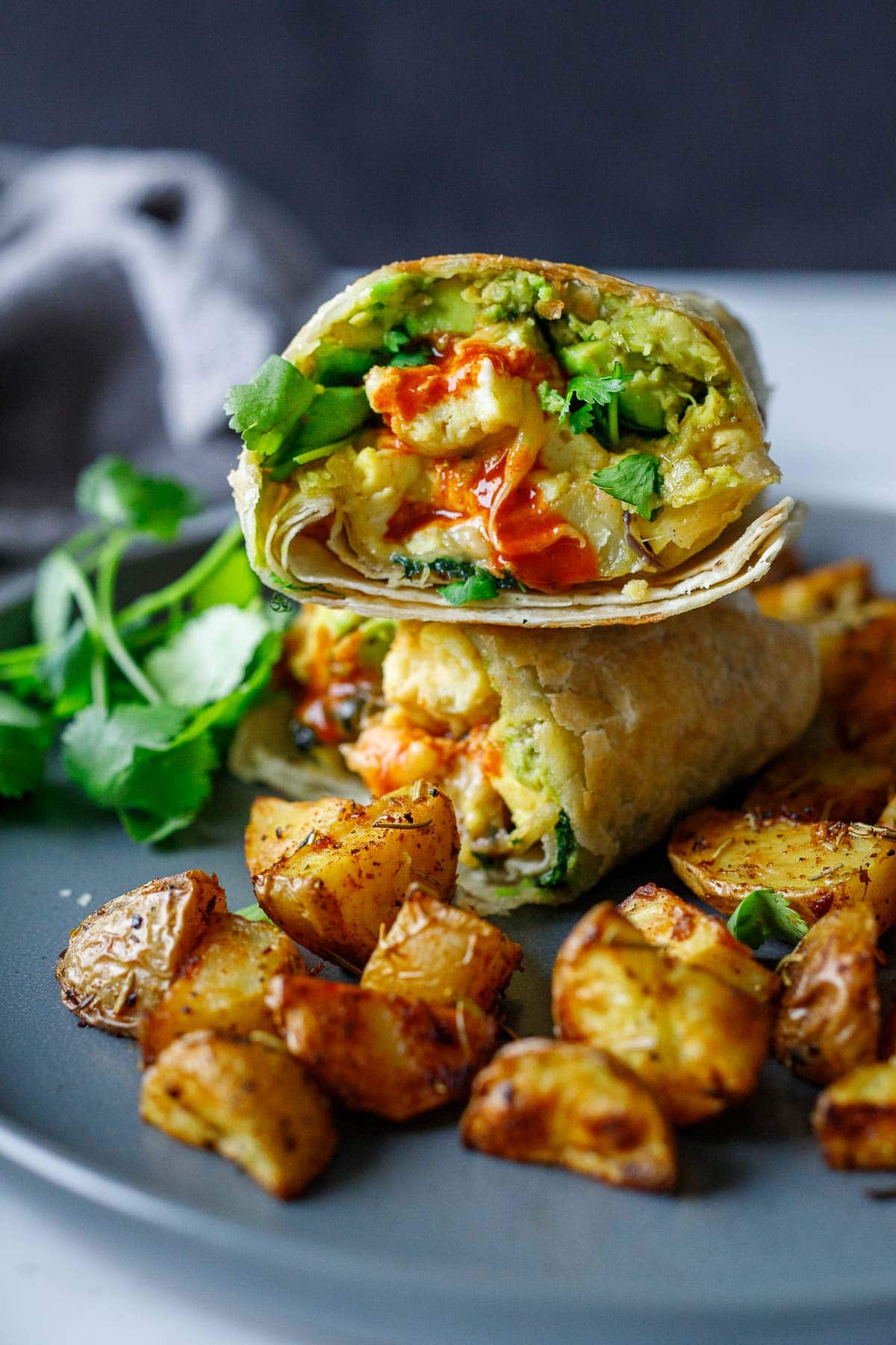 vegetarian breakfast burritos cut in half and stacked on plate with roasted potatoes.