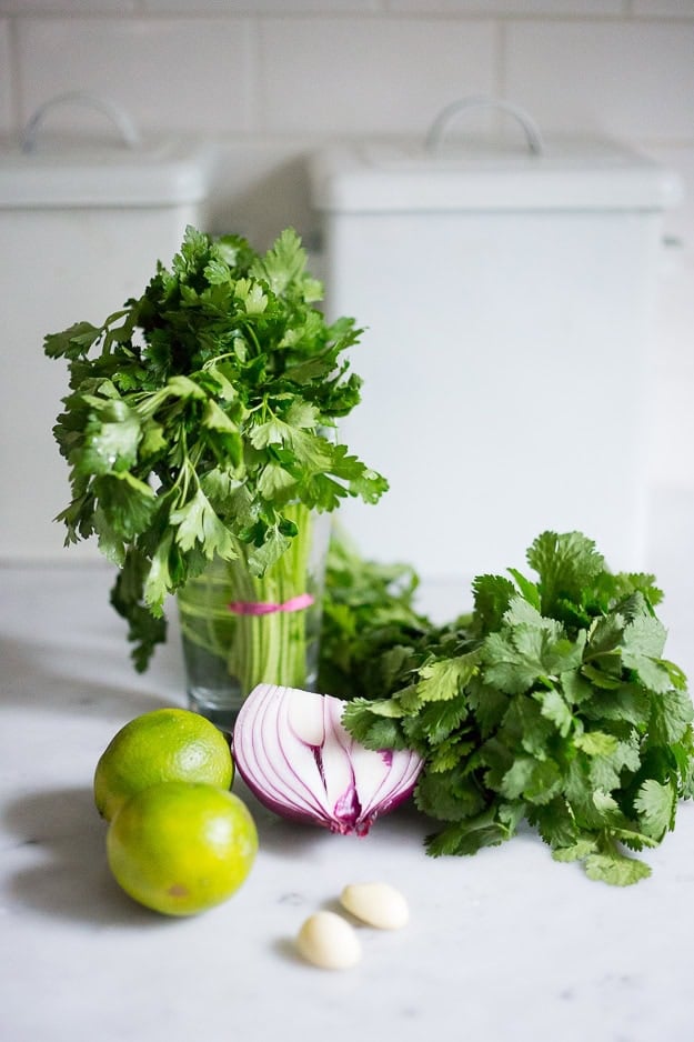 ingredients to make chimichurri sauce- cilantro, parsley, red onion, limes, garlic cloves.
