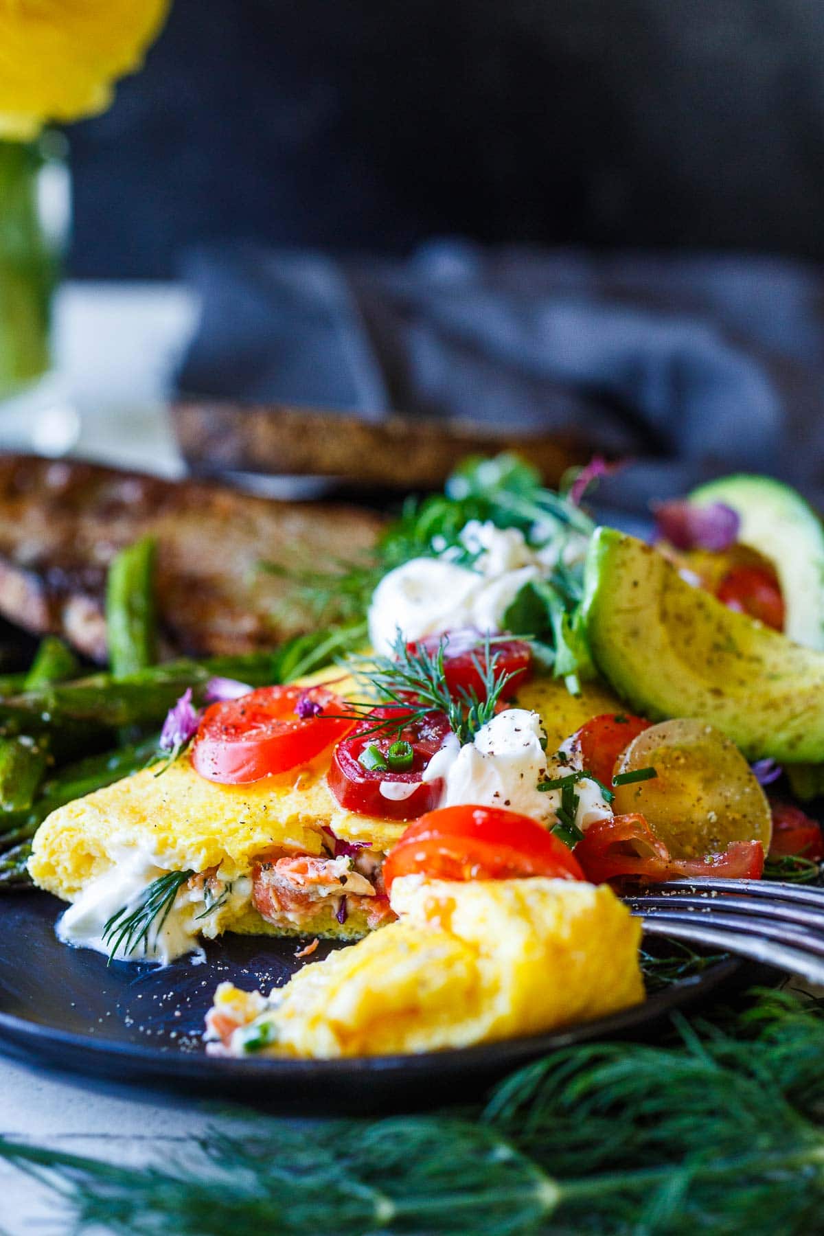 plate with champagne omelette cut open to show the salmon filling, topped with tomatoes, avocado, dill, chives, creme fresh.