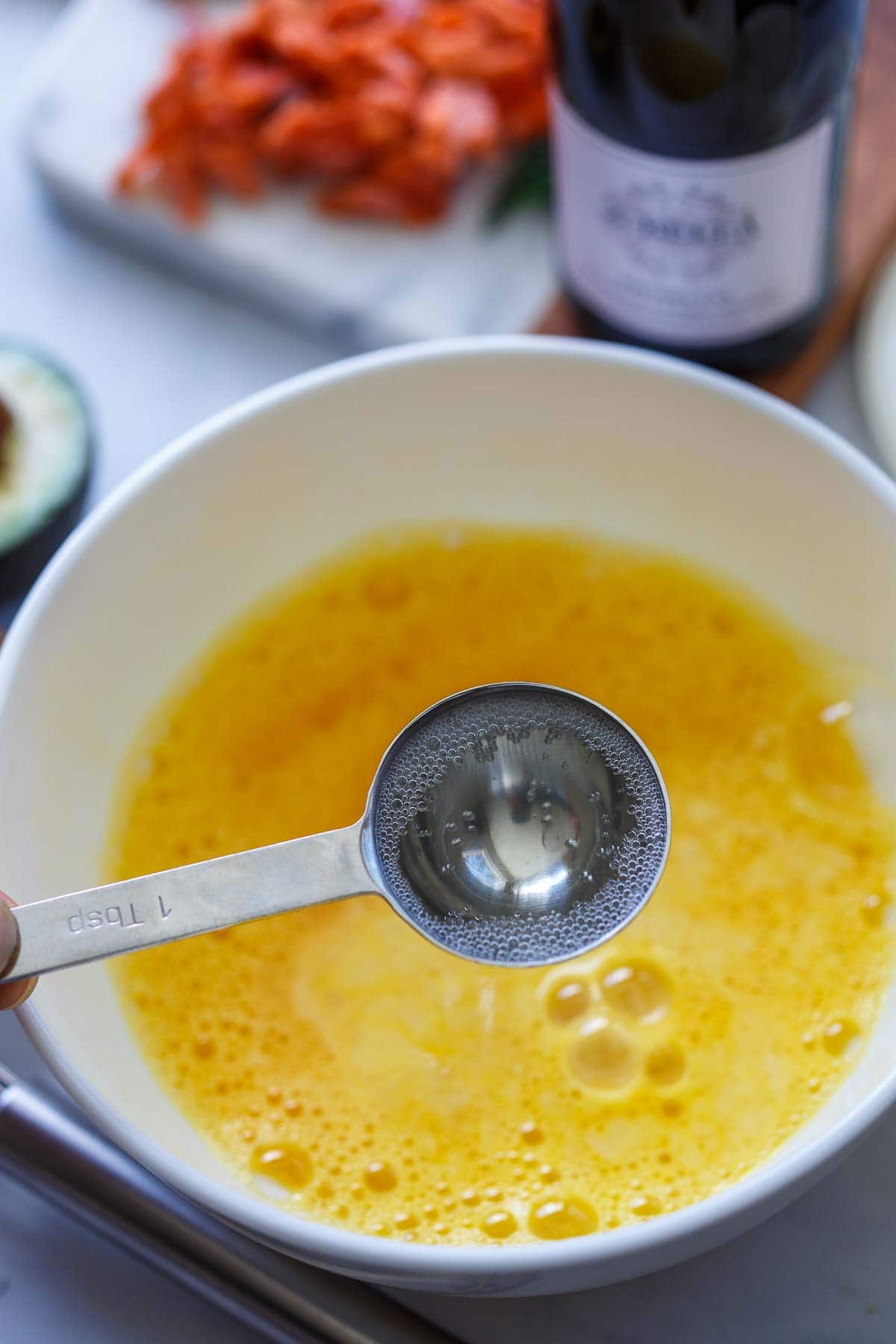 holding one tablespoon of champagne over bowl of whisked eggs.