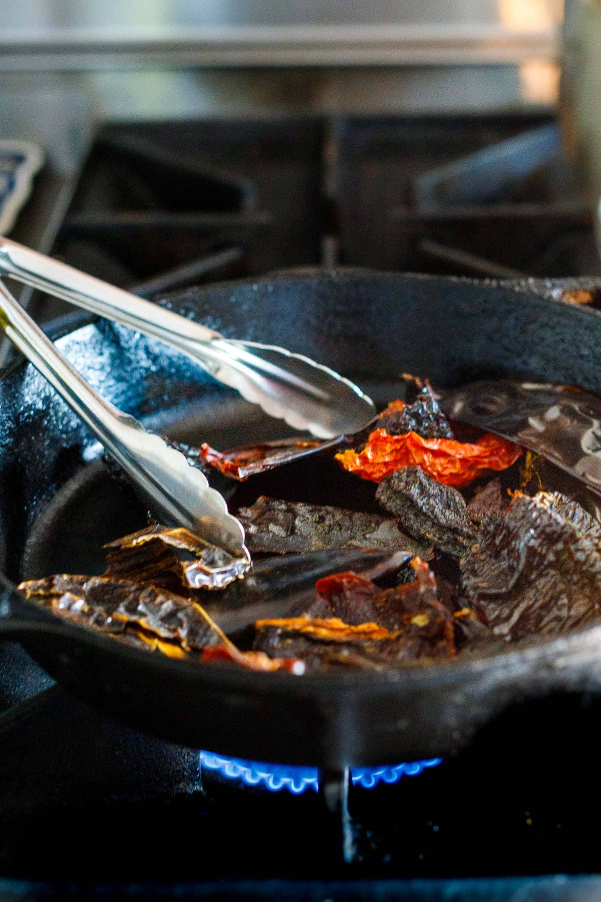 dried chiles toasting in cast iron skillet with tongs.