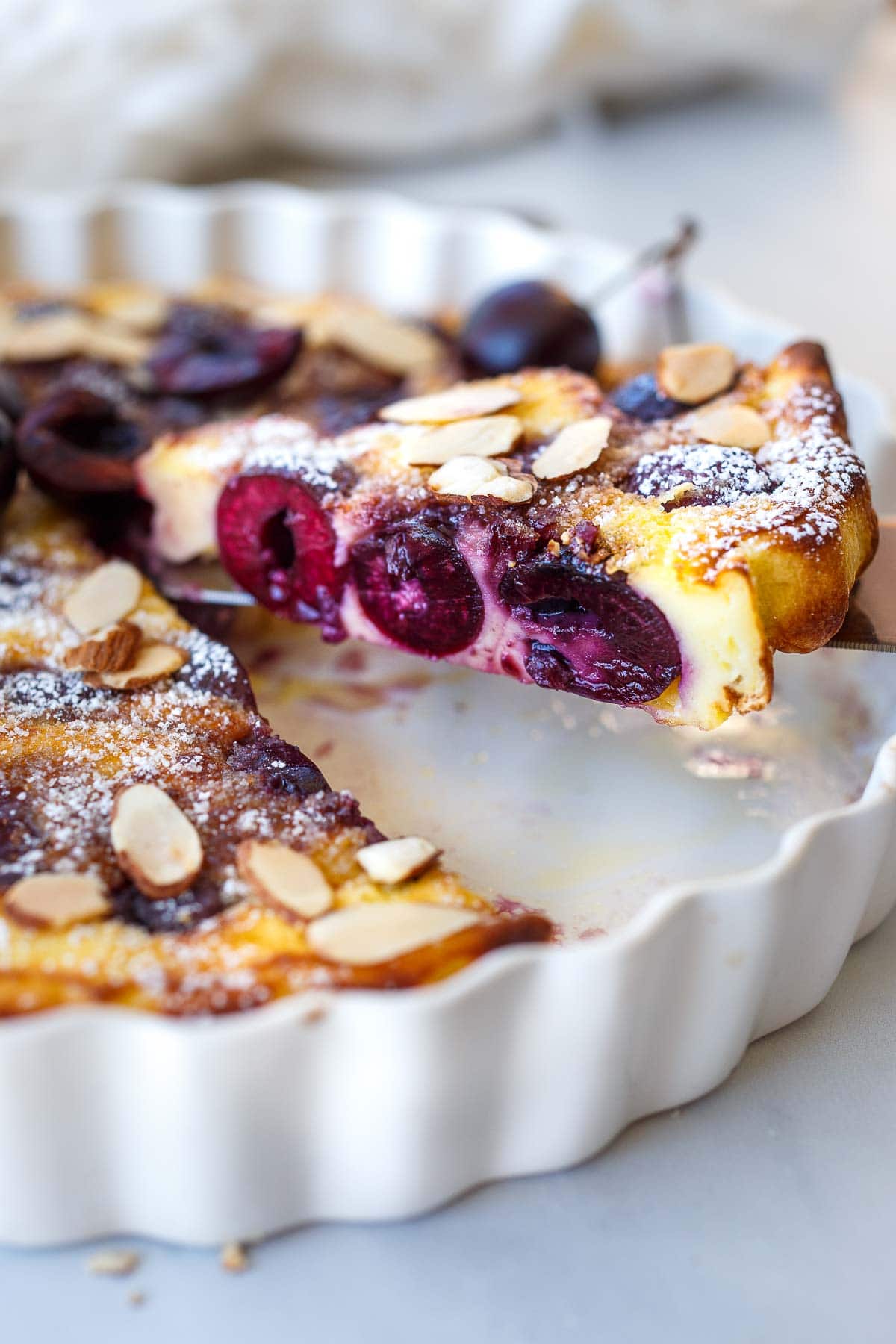 spatula lifting baked slice of cherry clafoutis from pan.