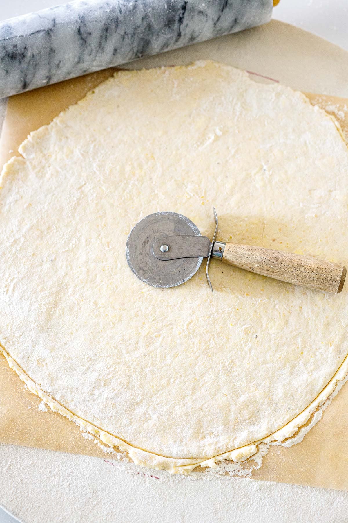 galette dough rolled into a round on parchment with pizza cutter on top.
