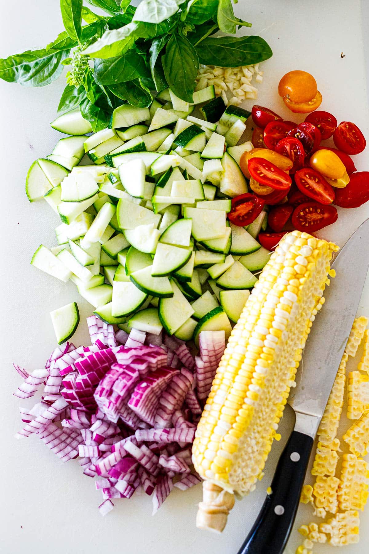 prepped veggies for the galette - basil, minced garlic, chopped zucchini and red onion, sliced cherry tomatoes, and sharp knife peeling off fresh corn.