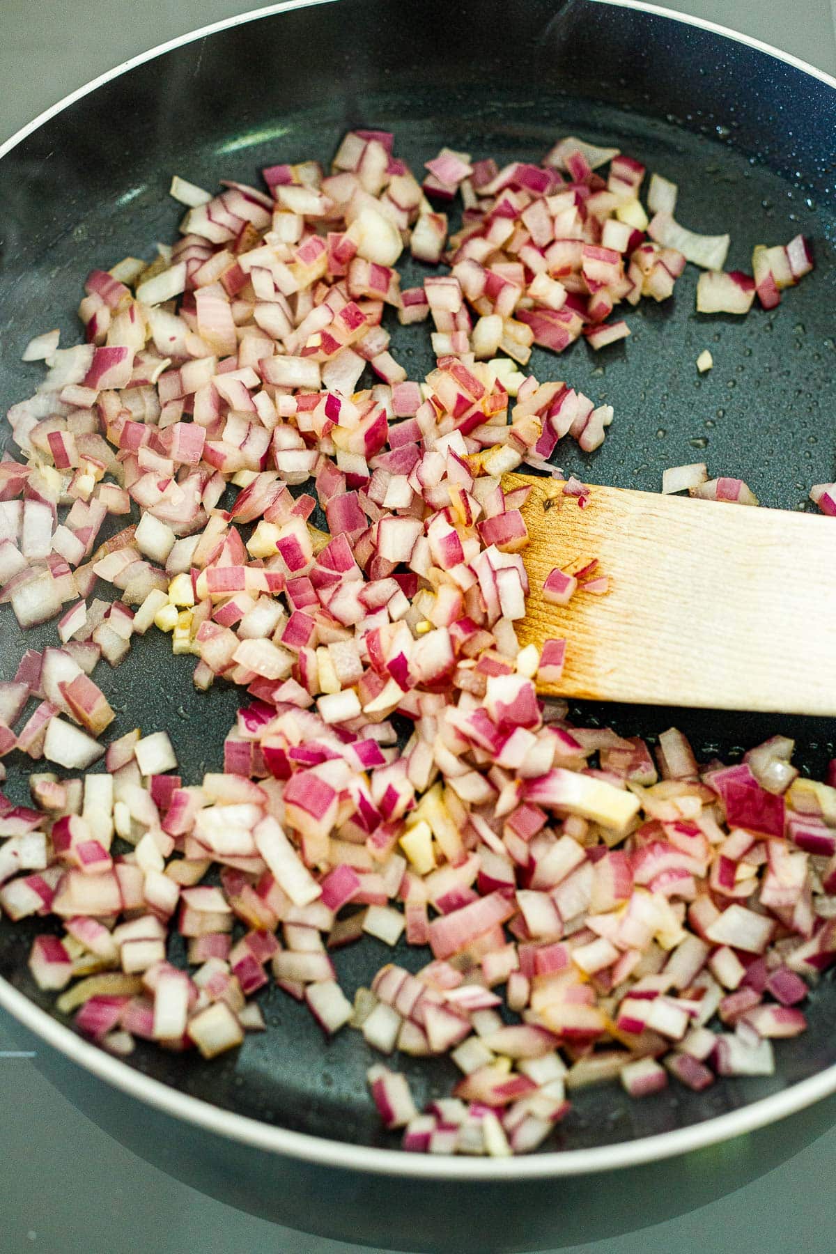 skillet and wooden spatula sauteing red onion.