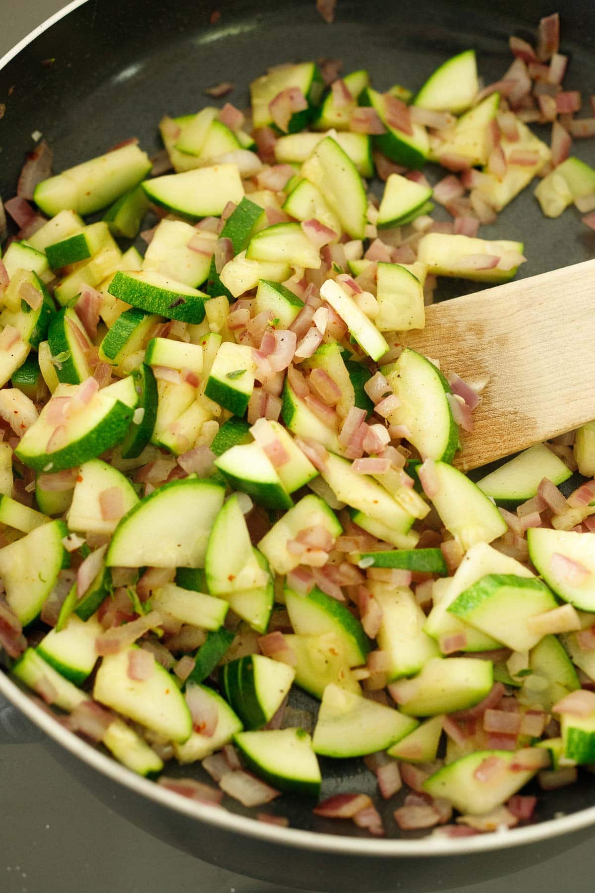 skillet and wooden spatula stirring sauteed zucchini and onion.