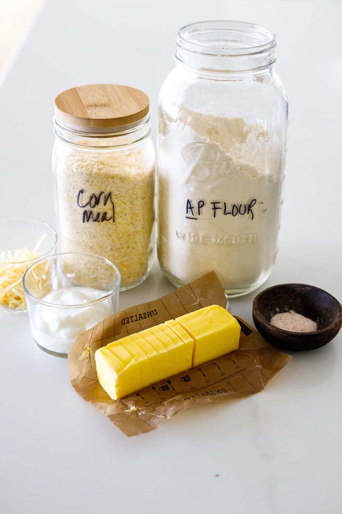 savory summer galette dough ingredients - jar of flour, corn meal, and dishes with cheese, yogurt, salt, and stick of butter sliced.