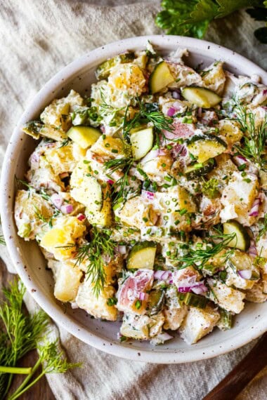 Light and creamy potato salad recipe with quick pickled cucumbers, fresh dill, and yogurt dressing in a white bowl.