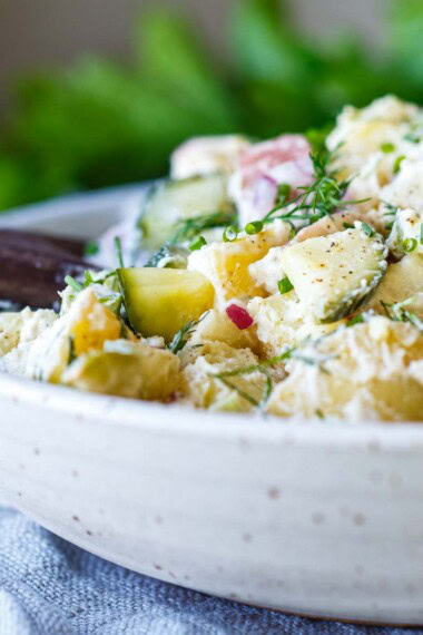 Light and creamy potato salad recipe with quick pickled cucumbers, fresh dill, and yogurt dressing in a white bowl.