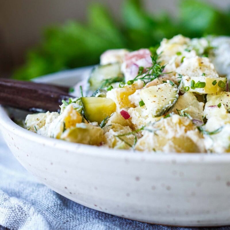 Light and creamy potato salad recipe with quick pickled cucumbers, fresh dill, and yogurt dressing in a white bowl.