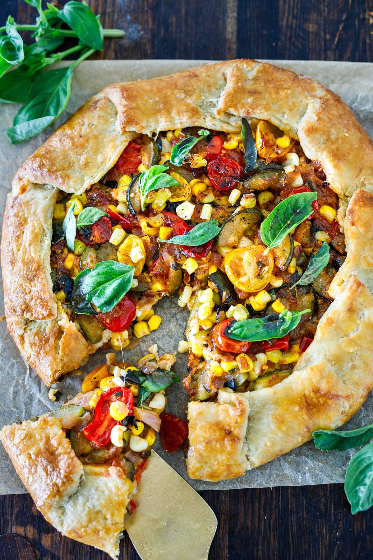 savory summer galette on parchment with slice being pulled out with pie spatula.