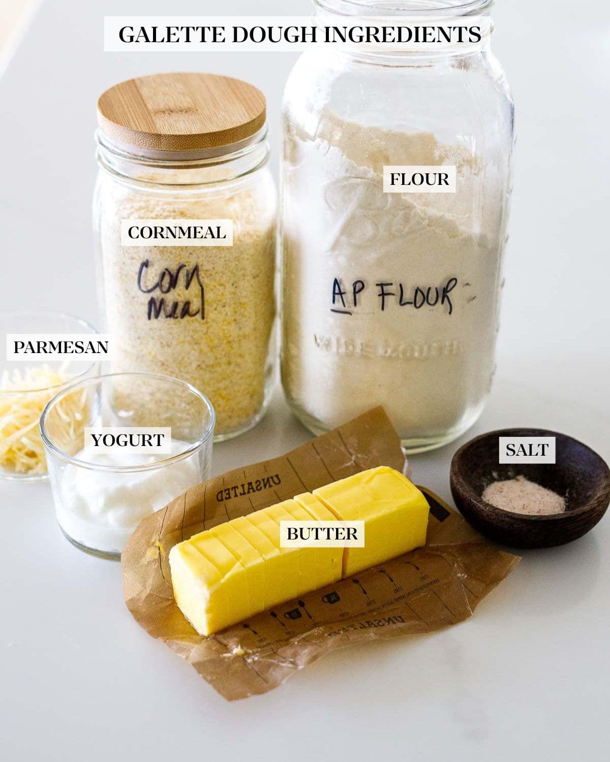 savory summer galette dough ingredients - jar of flour, corn meal, and dishes with cheese, yogurt, salt, and stick of butter sliced. 