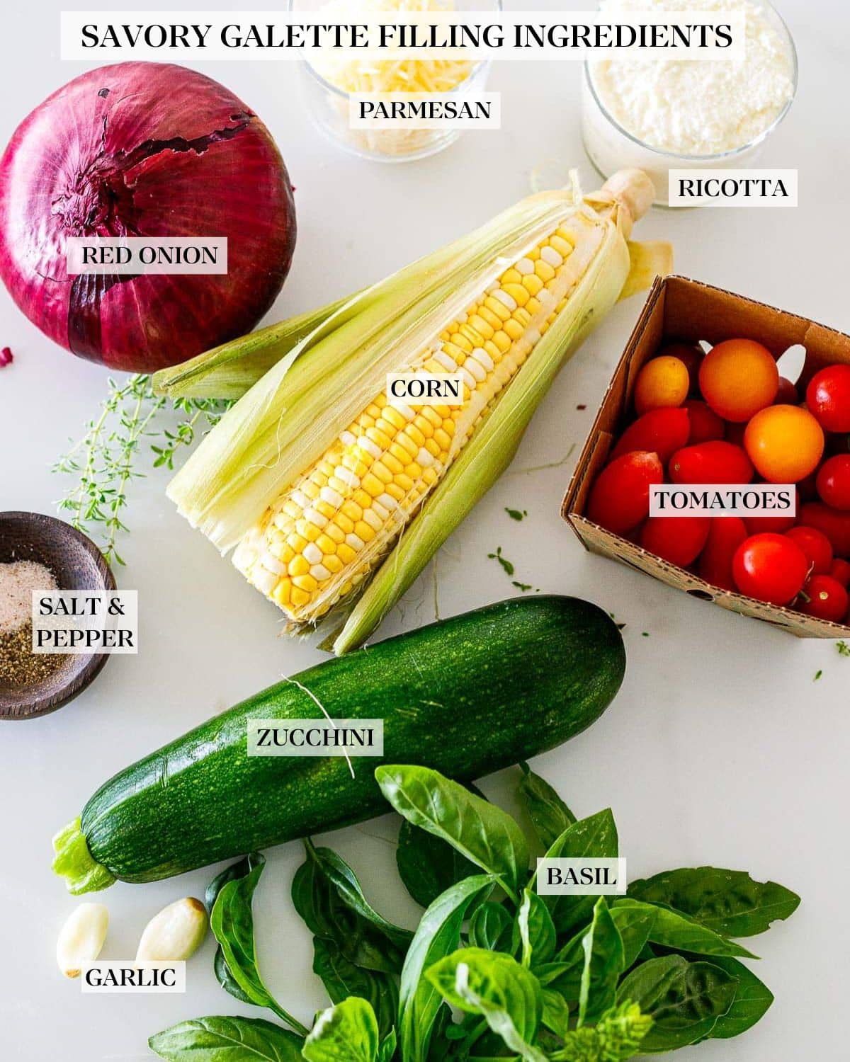 veggies laid out for savory summer galette filling- cherry tomatoes, zucchini basil, garlic, corn, and onion with jars of ricotta and parmesan. 