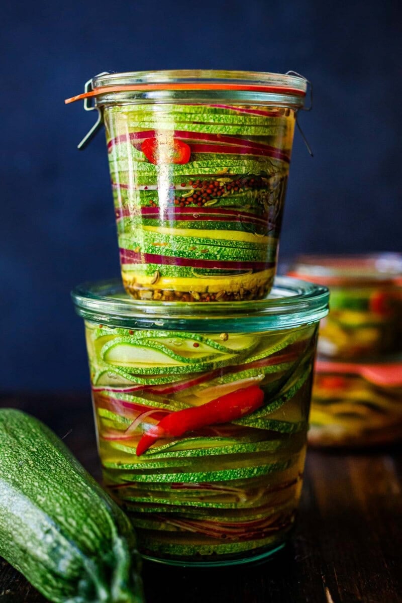 Zucchini pickles are delicious in sandwiches, burgers, or even just for snacking!  Easy to make and full of great flavor, this recipe makes great use of your late-summer harvest, preserving them for weeks in the fridge! They make a beautiful hostess gift as well!