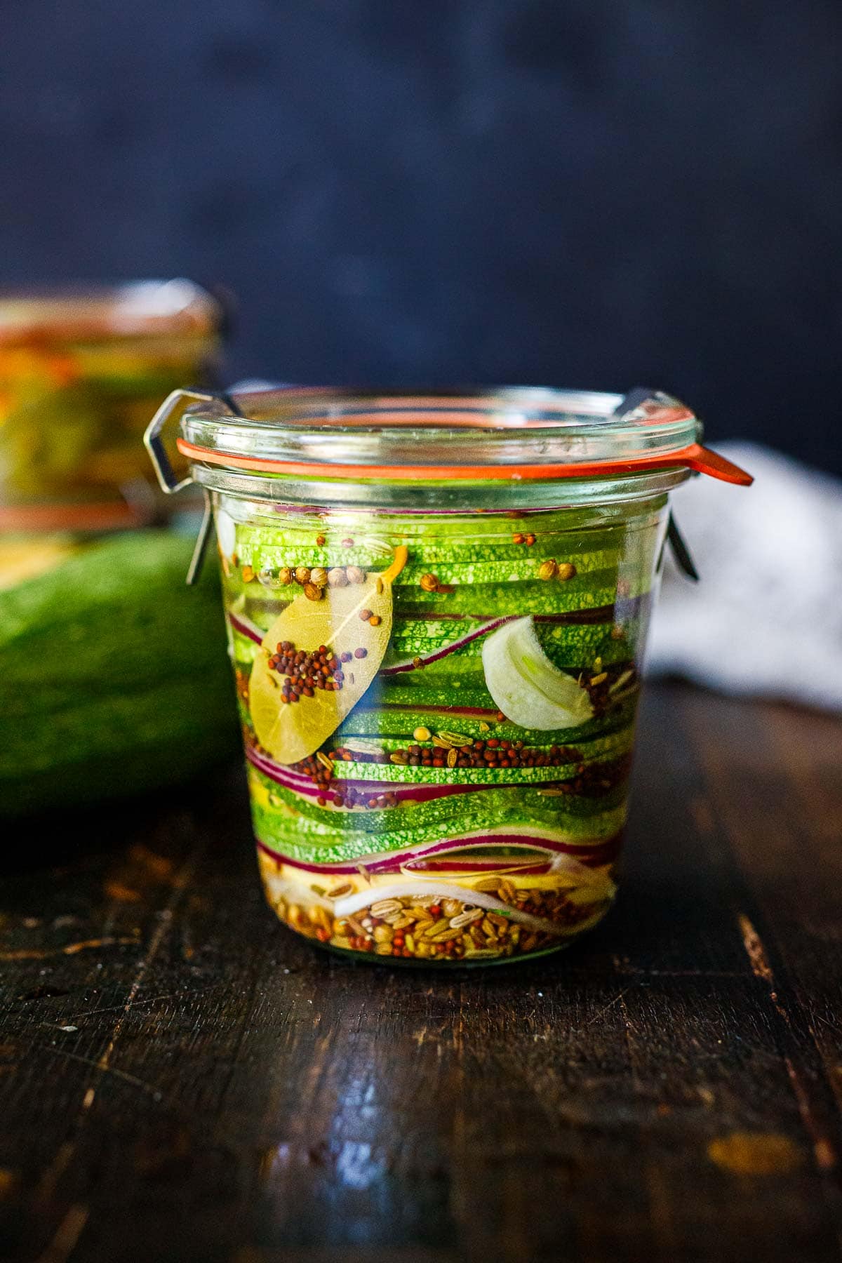 Zucchini pickles in a jar with bay leaves, garlic, seeds, onions.