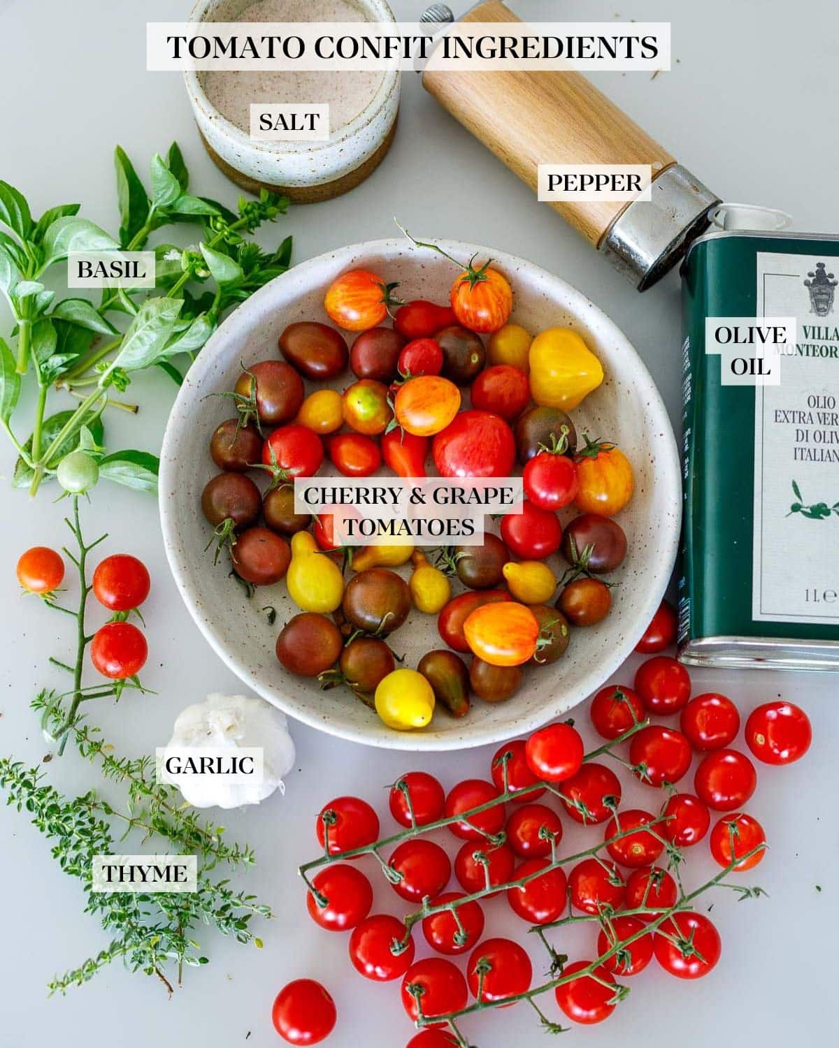 ingredients laid out for tomato confit - salt, pepper shaker, olive oil, bowl of mixed cherry tomatoes, basil, thyme, garlic.