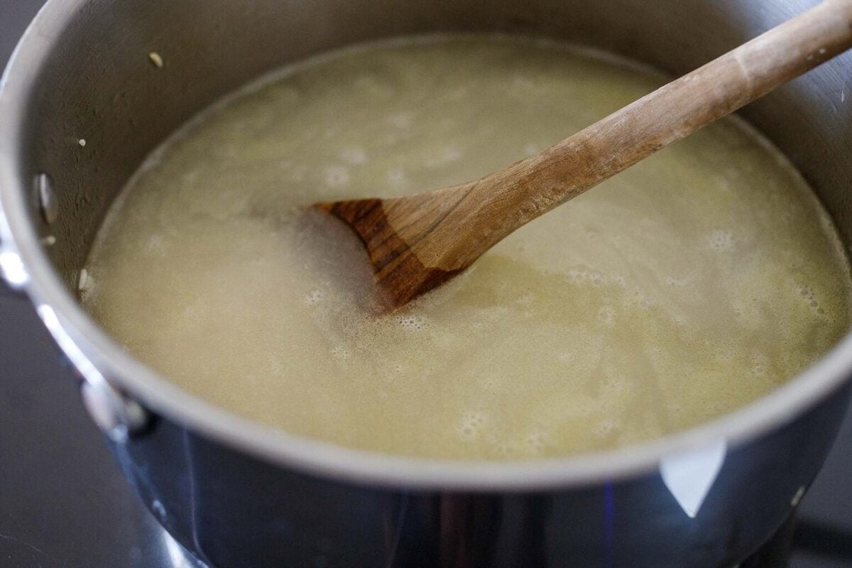 large pot with rice and water and a wood spoon to stir.