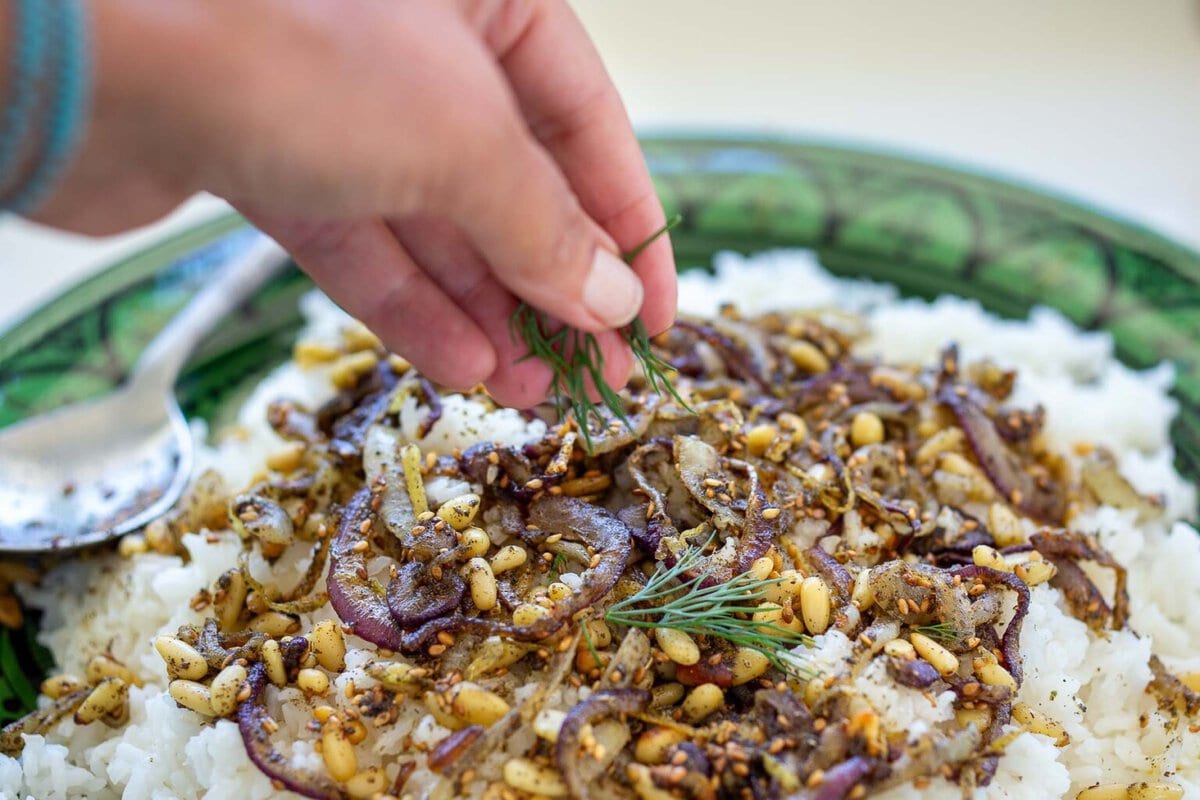 hand sprinkling fresh dill on top of middle eastern rice.