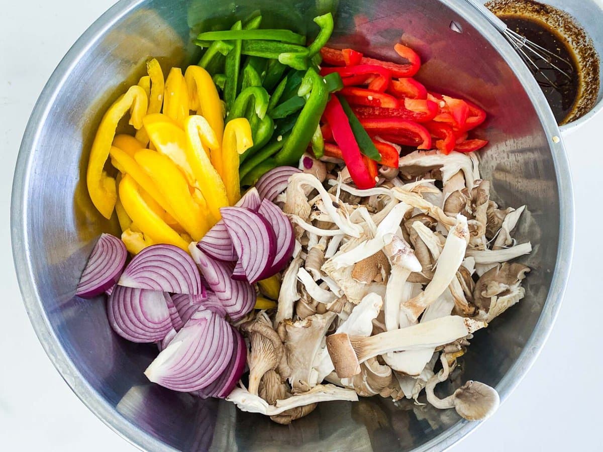 mixing bowl with sliced bell peppers and red onion and torn oyster mushrooms.