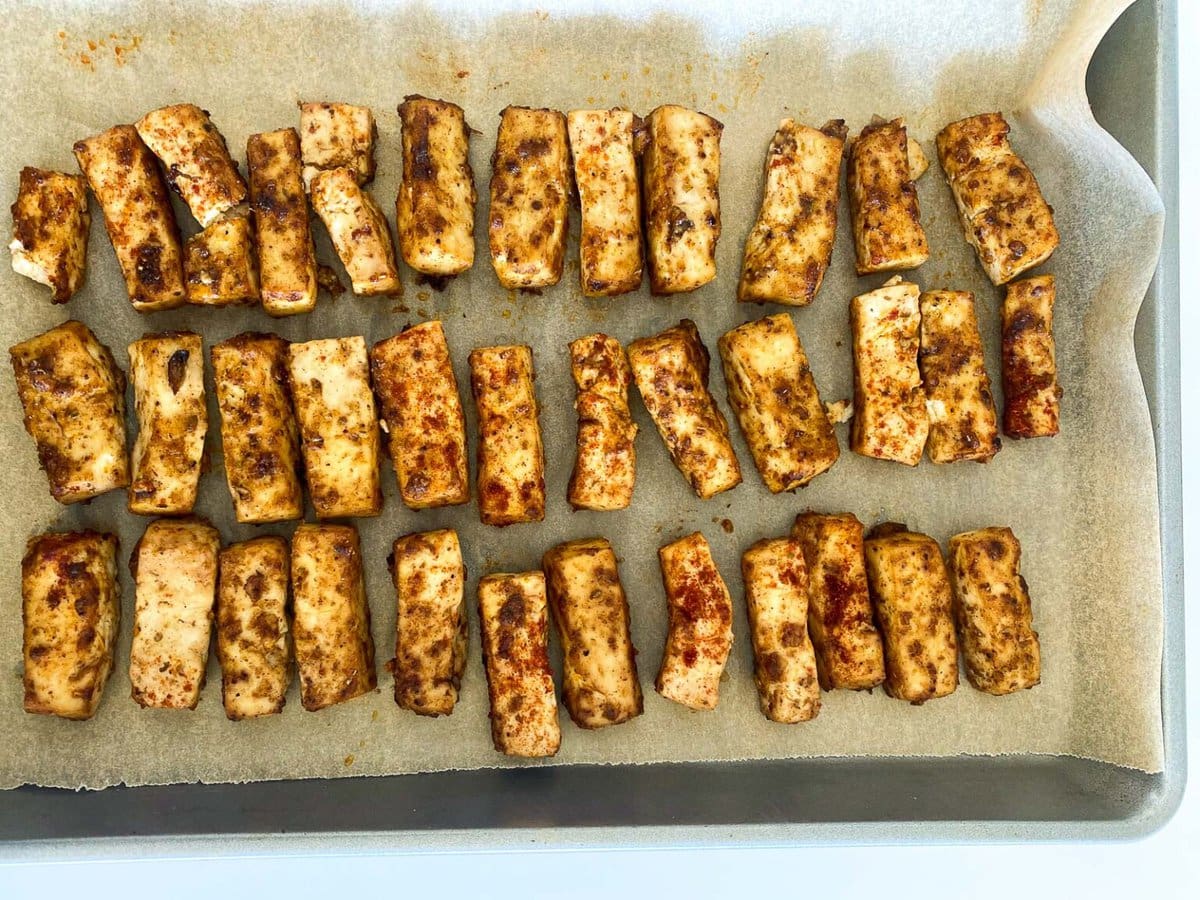parchment lined sheet pan with tofu pieces coated in marinade.