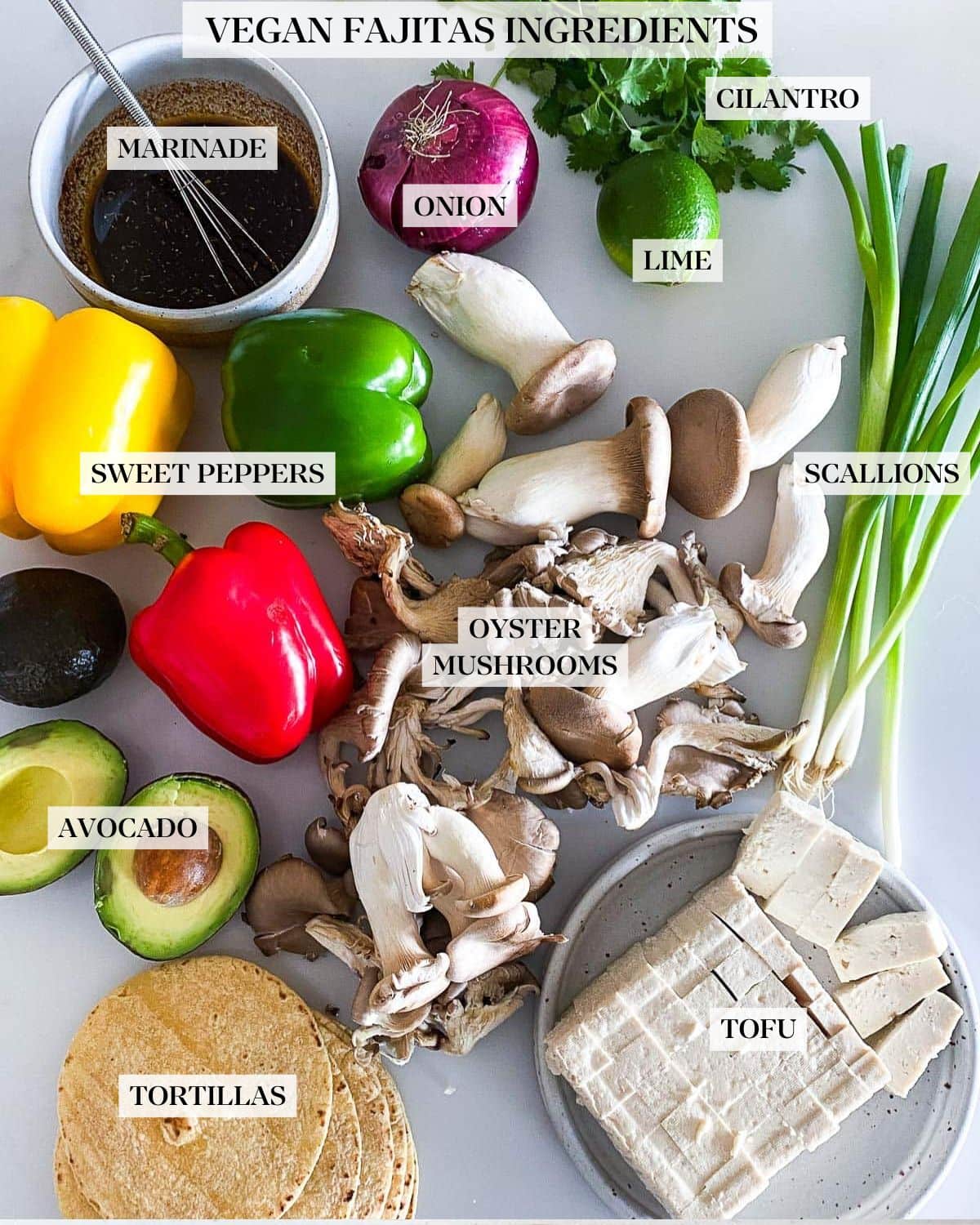 ingredients laid out for vegan fajitas - cilantro, lime, red onion, oyster mushrooms, bell peppers, green onions, avocado, marinade, tofu, and tortillas.
