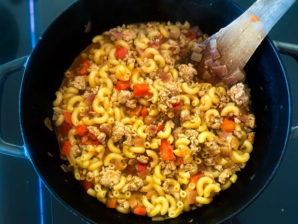 large pot of macaroni noodles with ground turkey and diced onions and peppers.