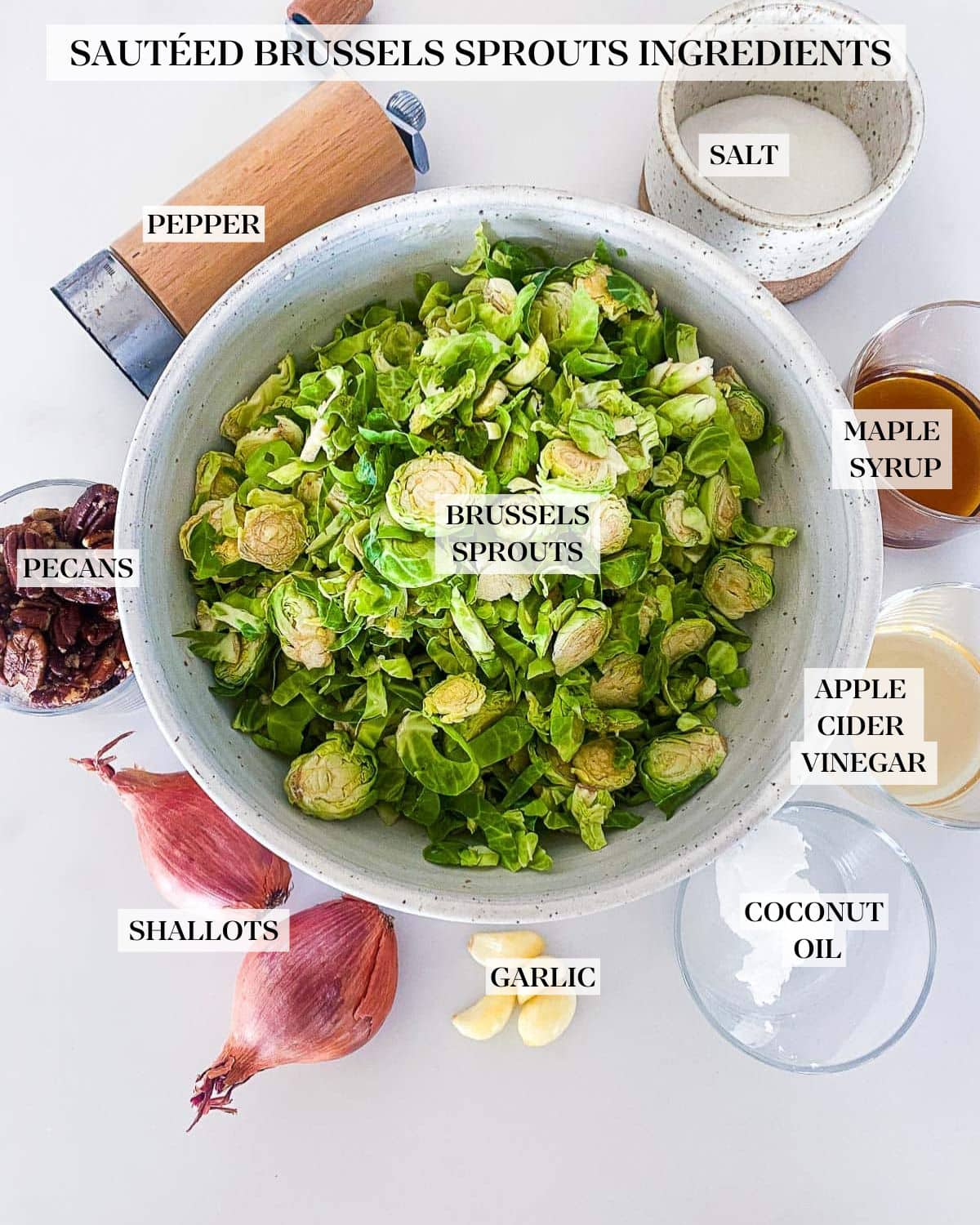 ingredients for sauteed Brussels sprouts laid out- bowl of shredded Brussels sprouts, pepper shaker, bowl of salt, maple syrup, apple cider vinegar, coconut oil, garlic cloves, shallot, and pecans. 