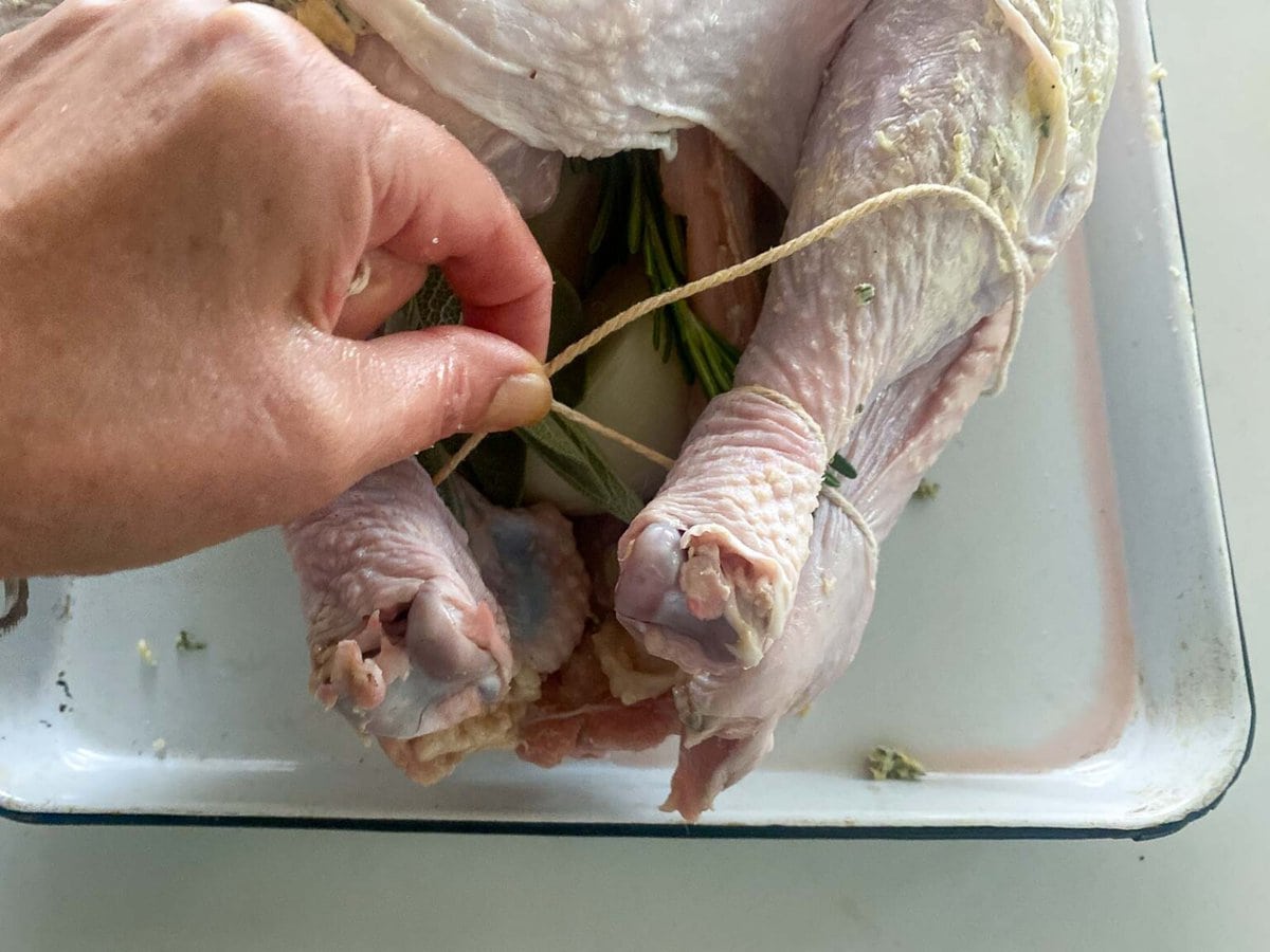 hand tying kitchen twine around turkey legs. 