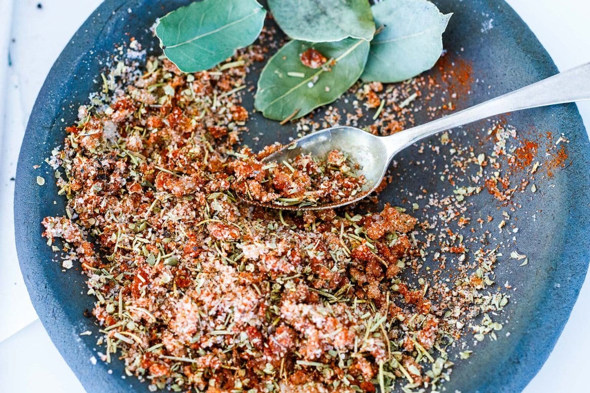 spoon mixing together spices for spice rub with bay leaves off to the side.