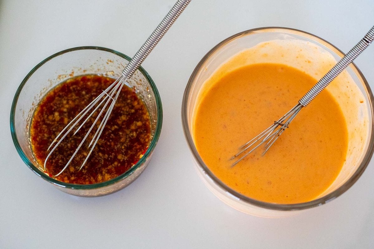 glass bowl with sticky sauce and whisk and glass bowl with yum yum sauce and whisk.