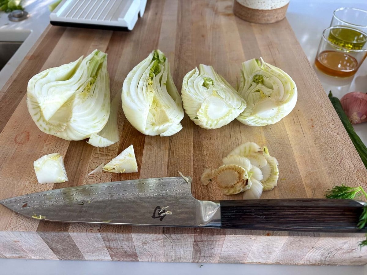 wood cutting board with sharp knife and fennel bulbs with cores cut out. 