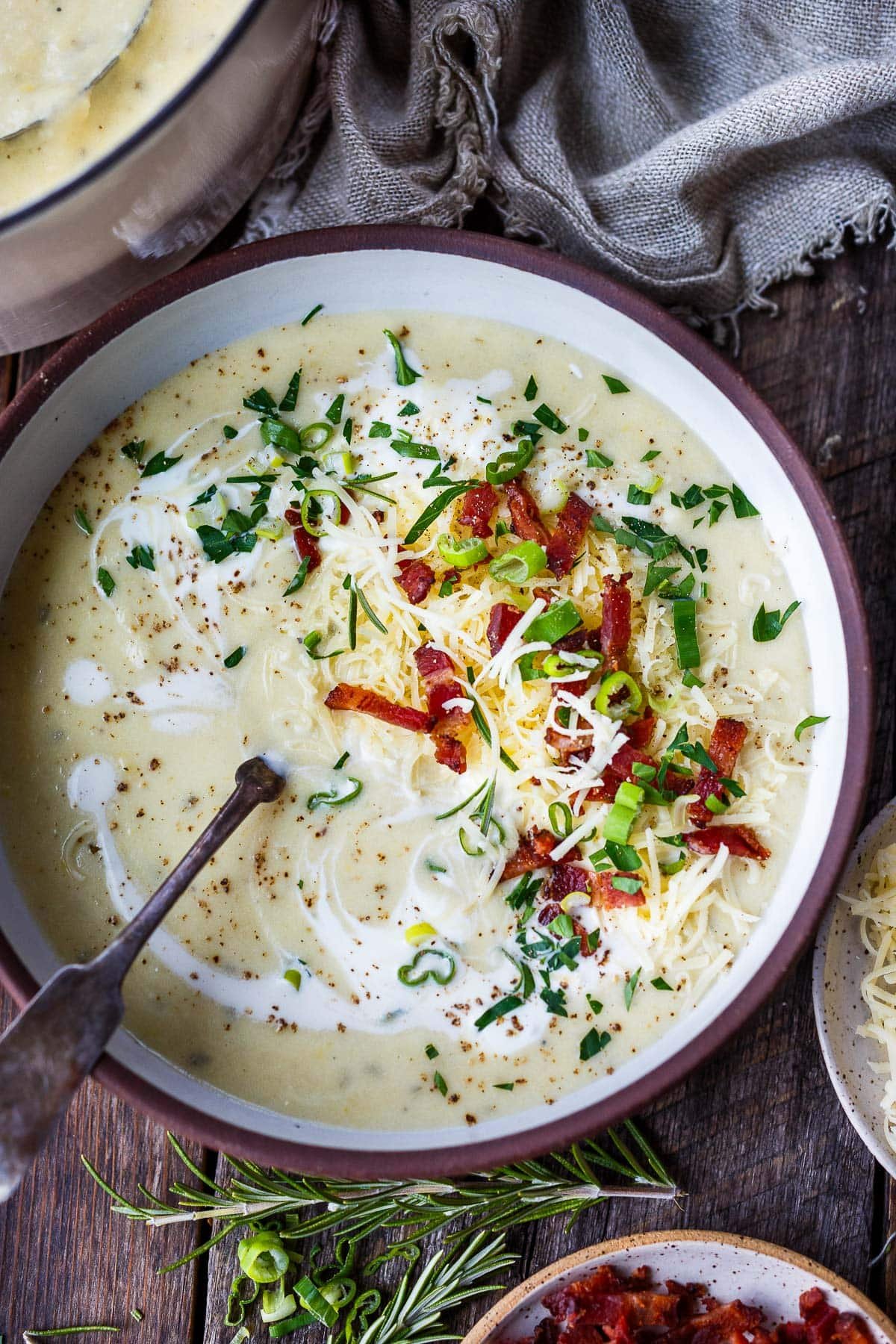 A bowls of potato soup with green onion, sour cream and bacon bits.