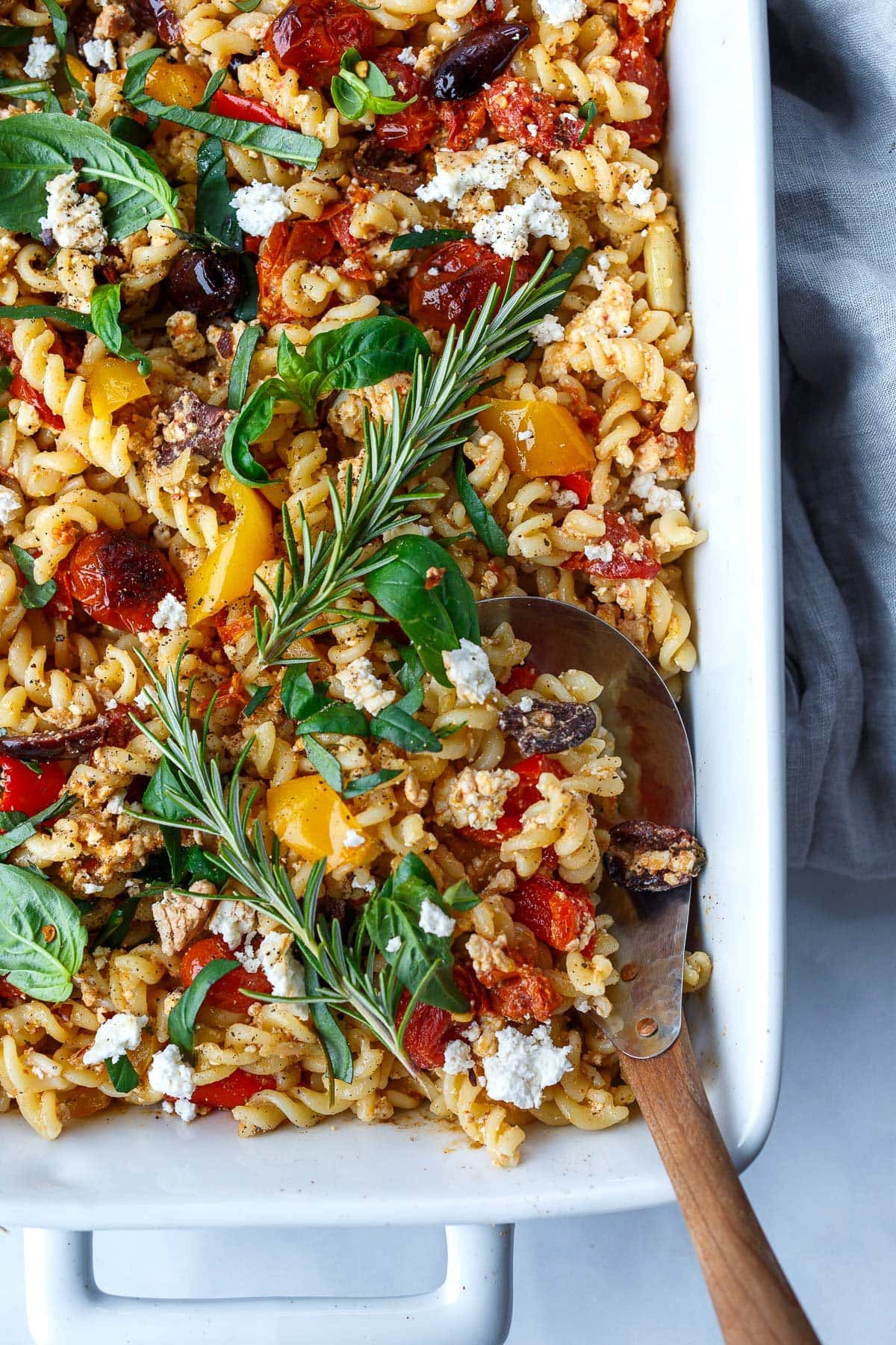 baked feta pasta in a rectangular baking dish with tomatoes, olives, and herbs.