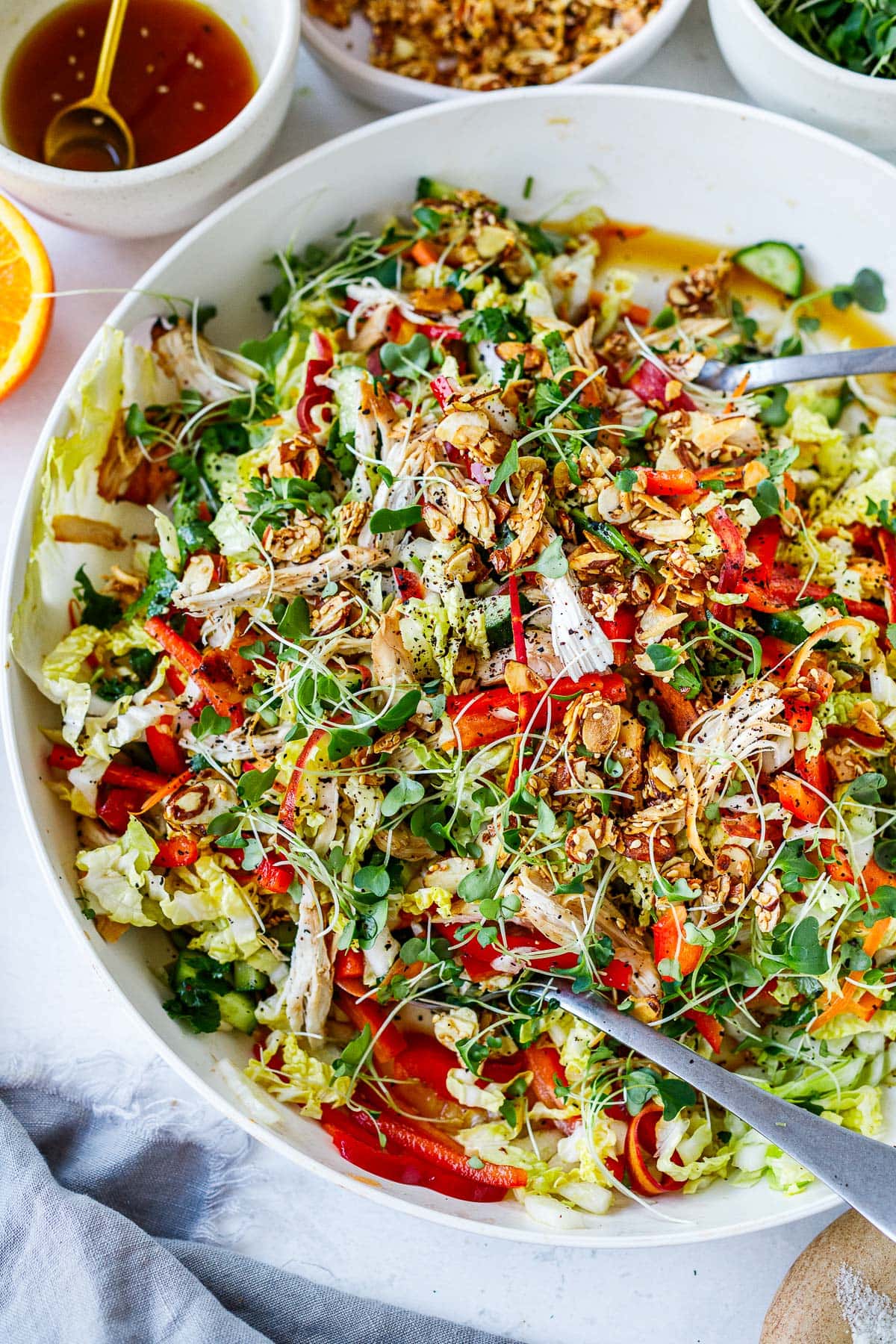 large salad bowl with chinese chicken salad with sesame almond brittle and two serving spoons.