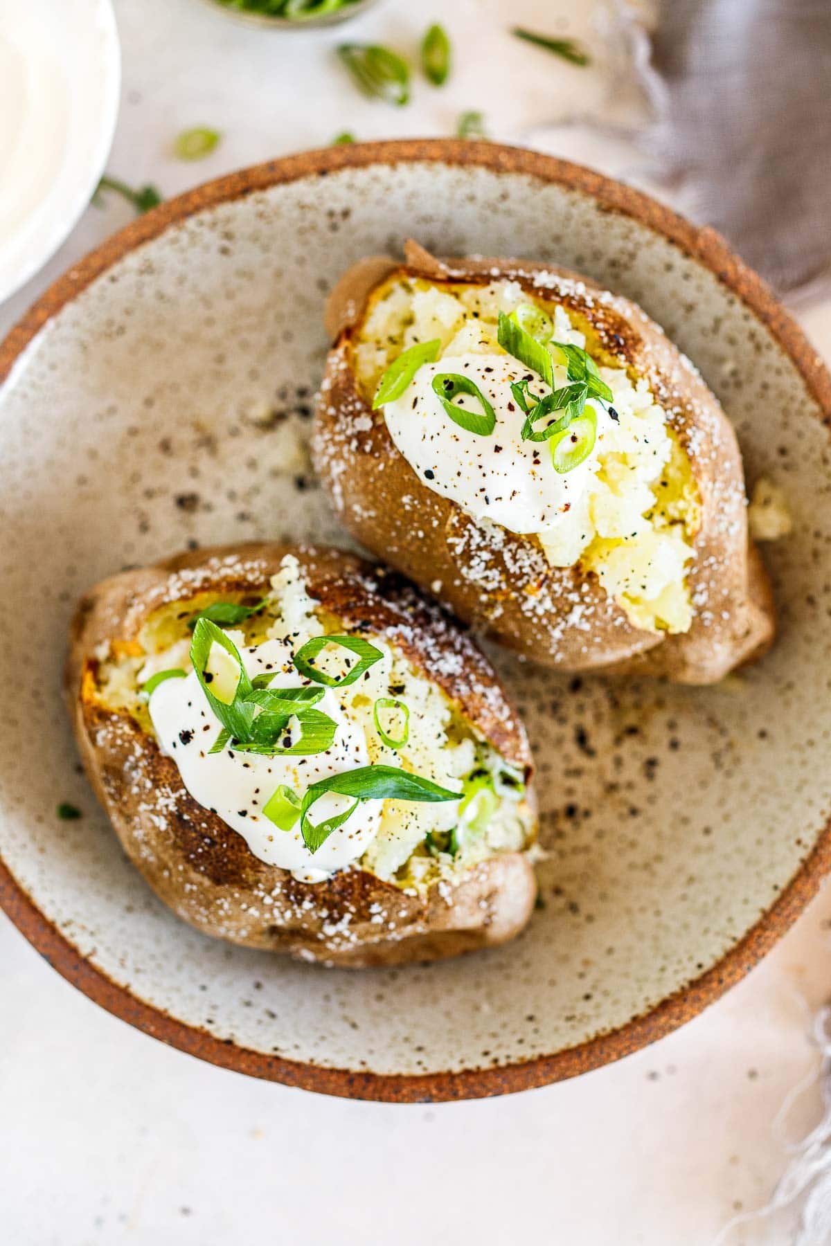 two baked potatoes with sour cream, green onions, and black pepper.