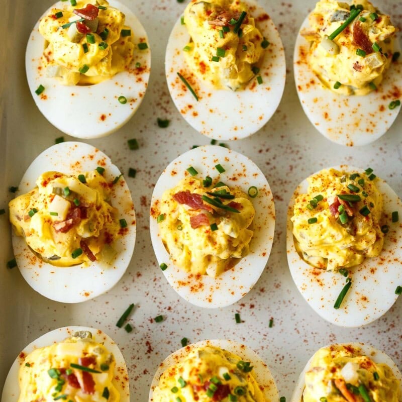 These deviled eggs (also known as Oeufs Mimosa) have the best texture and flavor! They are creamy and delicious, studded with crispy bacon (or vegan bacon), aged cheddar cheese, diced pickles, and sweet onions. The perfect low-carb appetizer, perfect for gatherings!