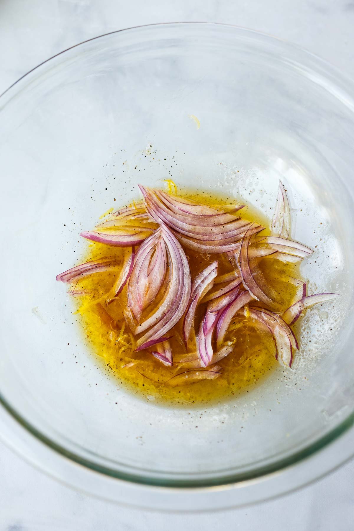 glass mixing bowl with dressing and thinly sliced red onion. 