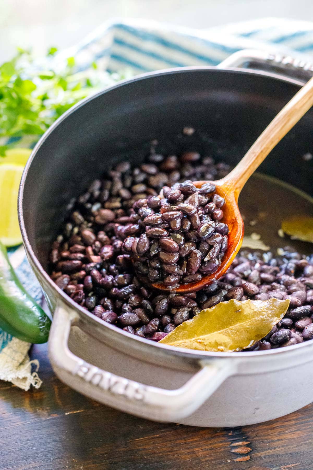 dutch oven with cooked black beans and a bay leaf, and a wood spoon lifting the beans from the pot.