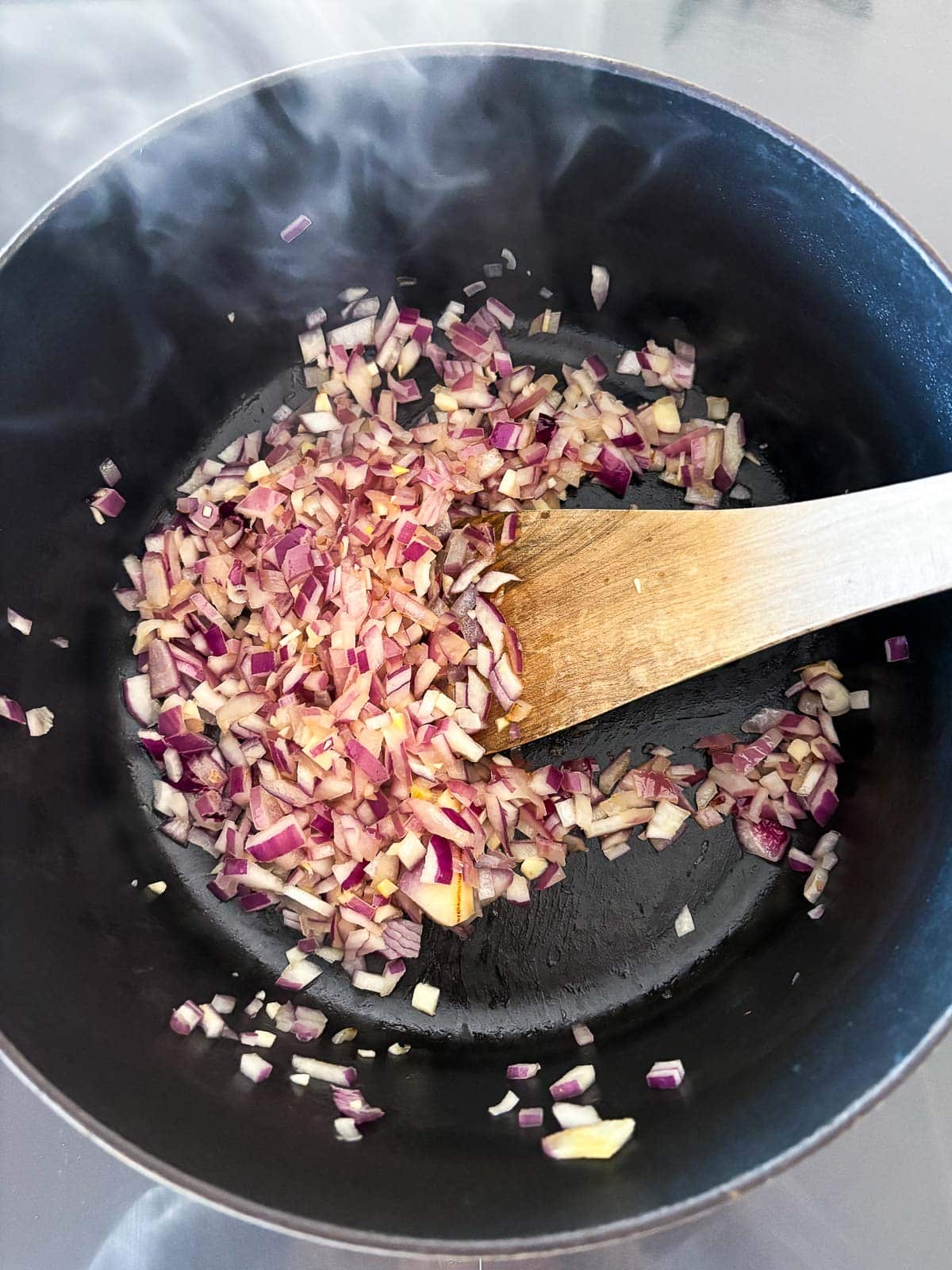 wood spoon stirring dutch oven with diced red onions.