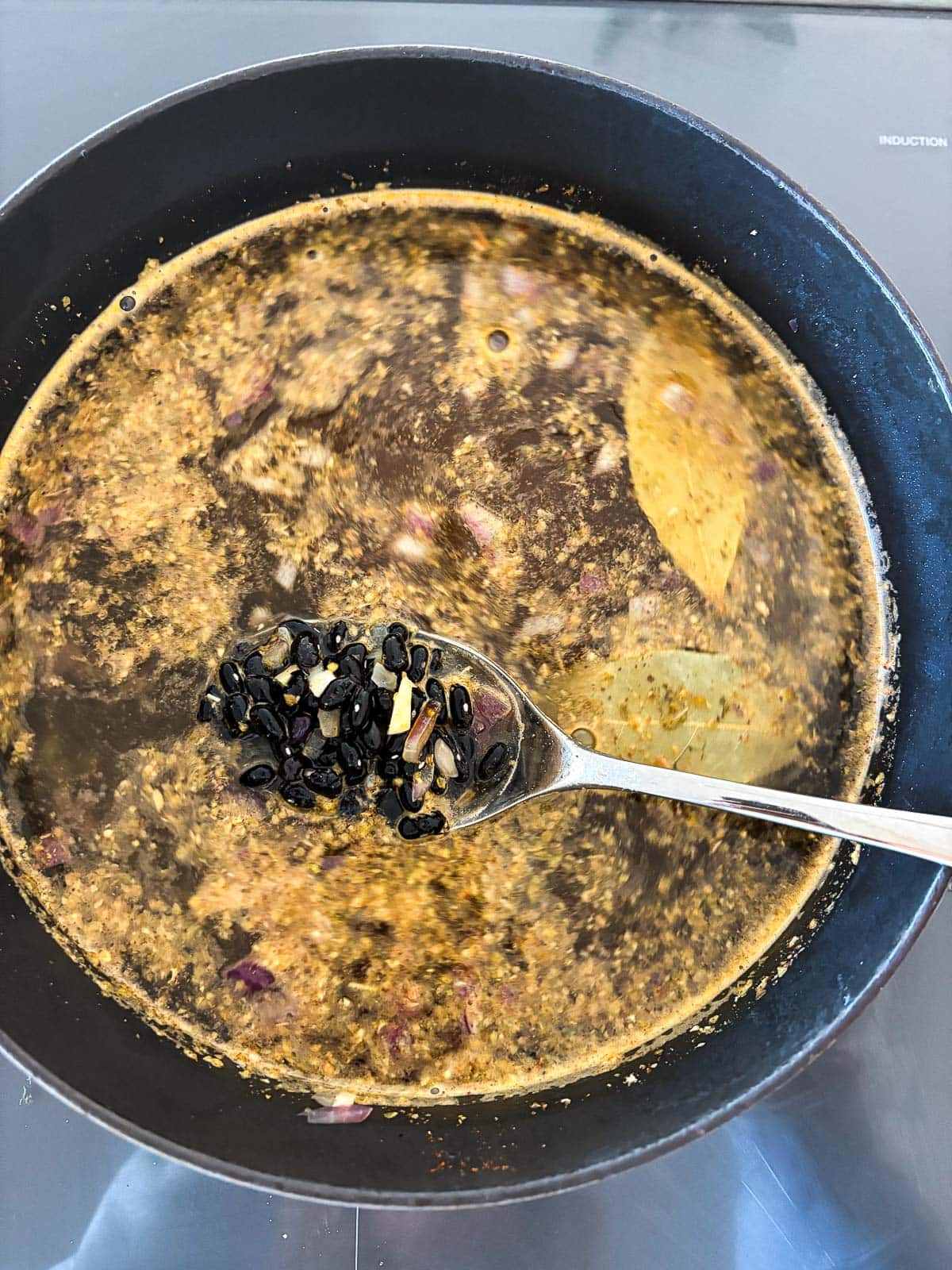dutch oven with broth and seasonings to cook black beans with silver spoon lifting black beans out of the pot.