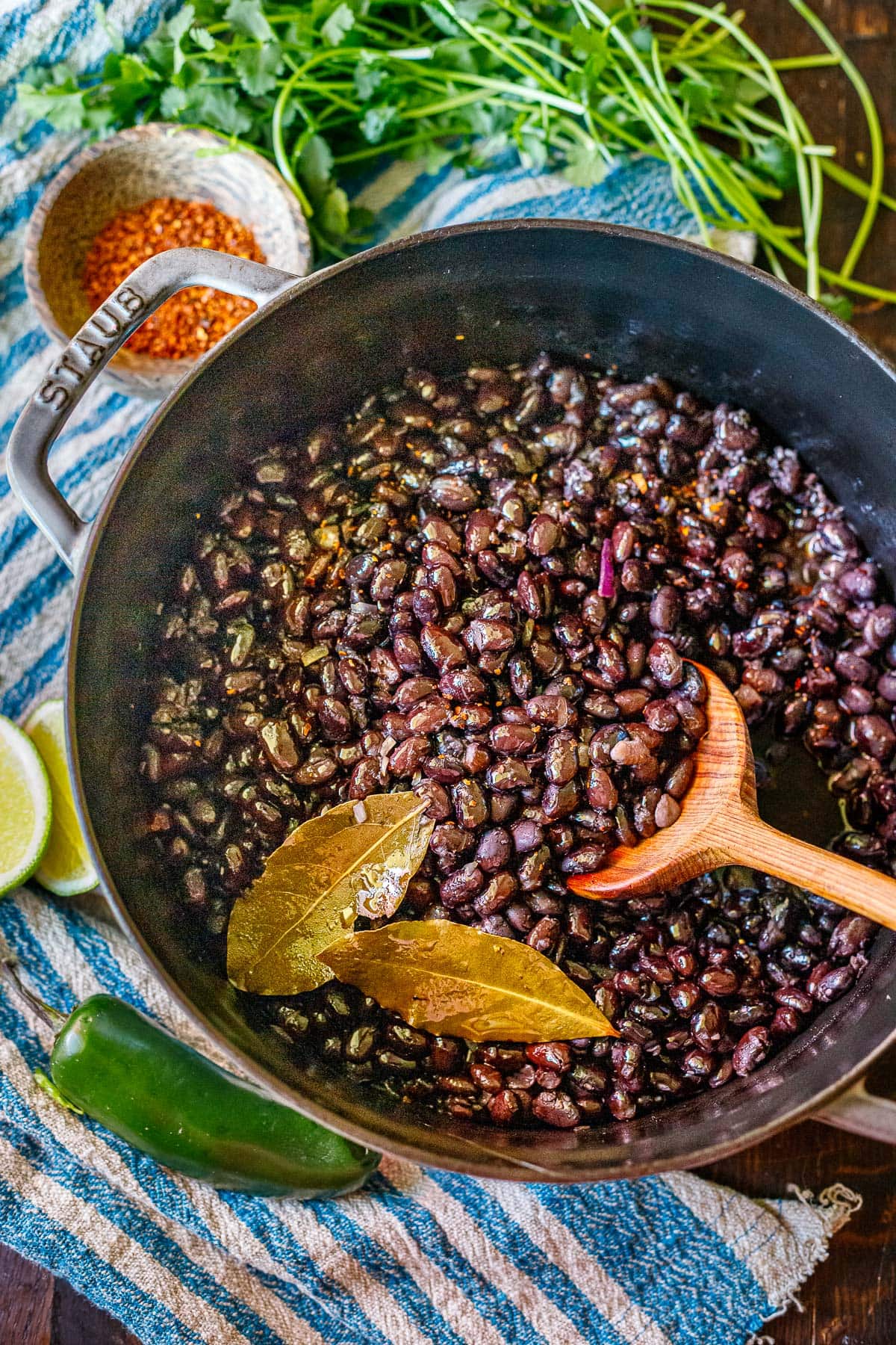 dutch oven with cooked black beans in pot with two bay leaves and a wood spoon.