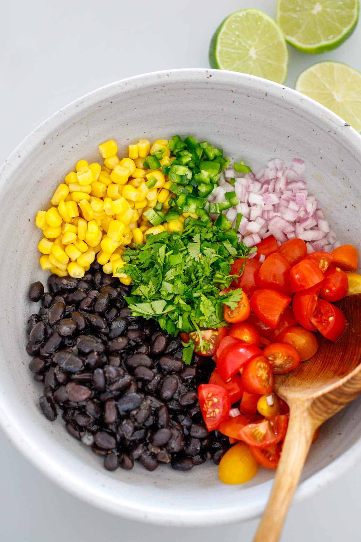 mixing bowl of black beans, corn, jalapeño, onion, cherry tomatoes, and cilantro before mixing to make black bean salsa.