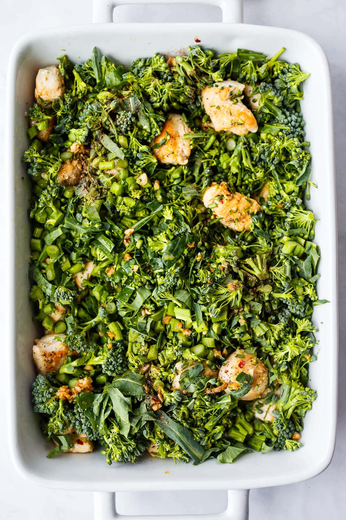 white rectangular ceramic baking dish with broccoli pieces and pieces of seared chicken breast. 