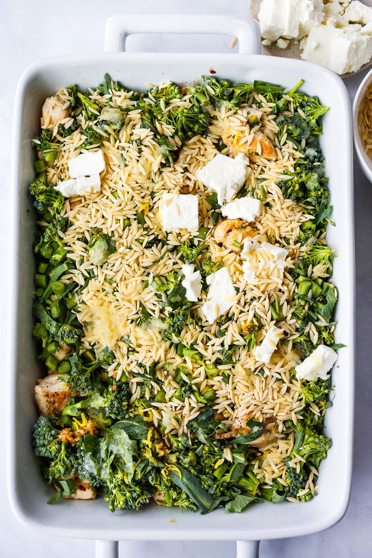 the chicken orzo bake before going in the oven with dry orzo pasta, pieces of feta cheese, broccoli, and seared chicken breast.