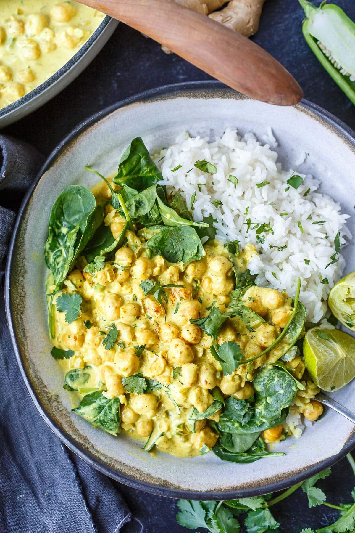 bowl of chickpea curry on jasmine rice with fresh spinach and lime wedges.