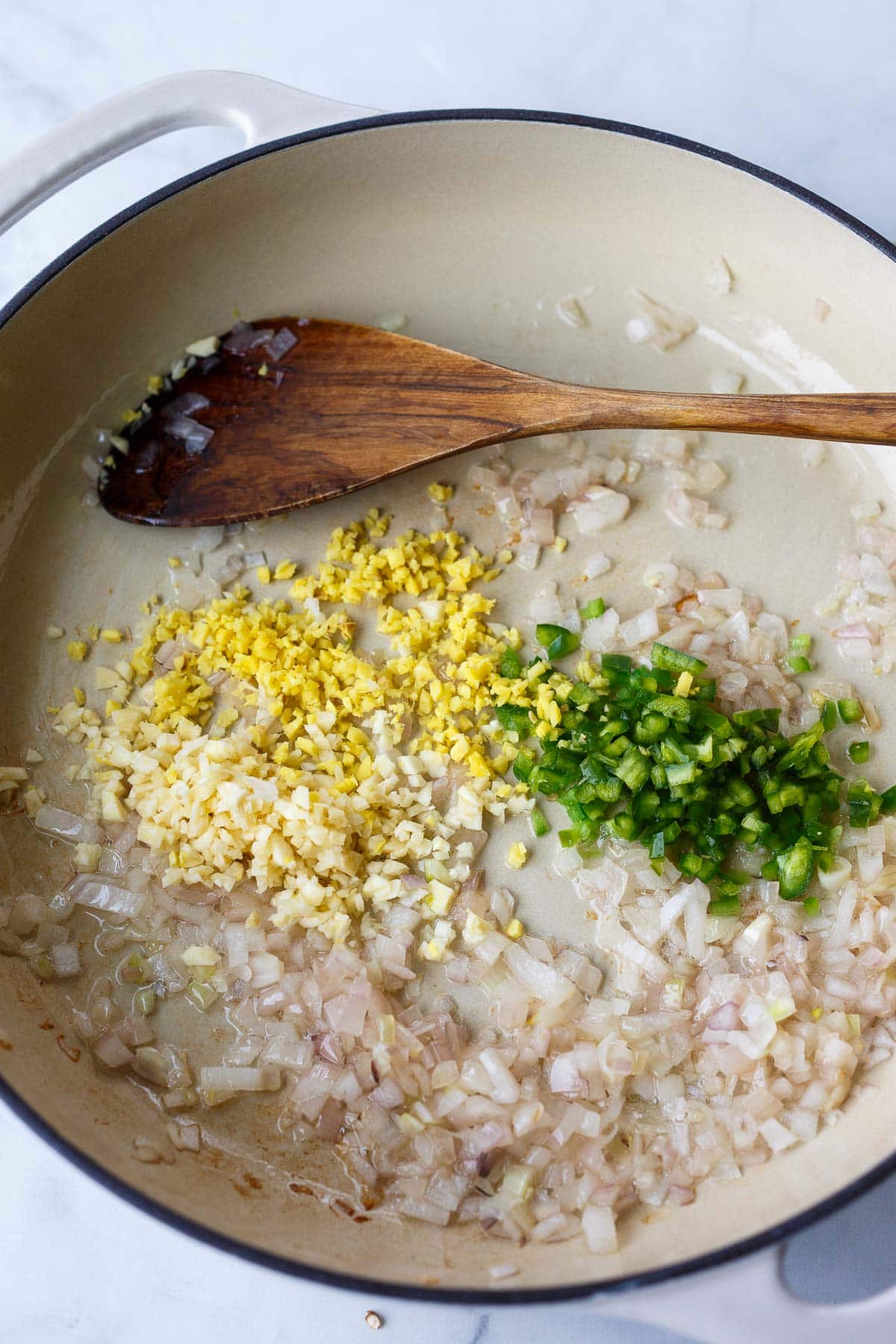 large pan with minced shallot, jalapeno, garlic, and ginger sautéing in coconut oil with wood spatula.