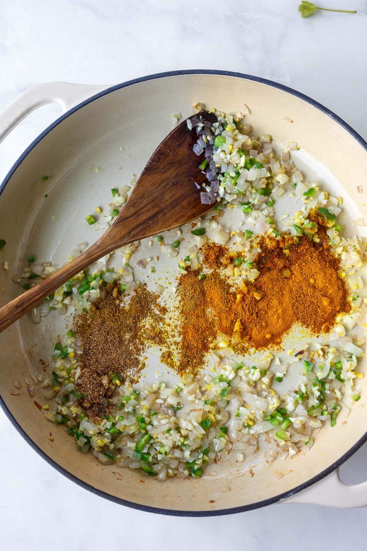 wood spoon stirring aromatics with spices for chickpea curry in large pan.