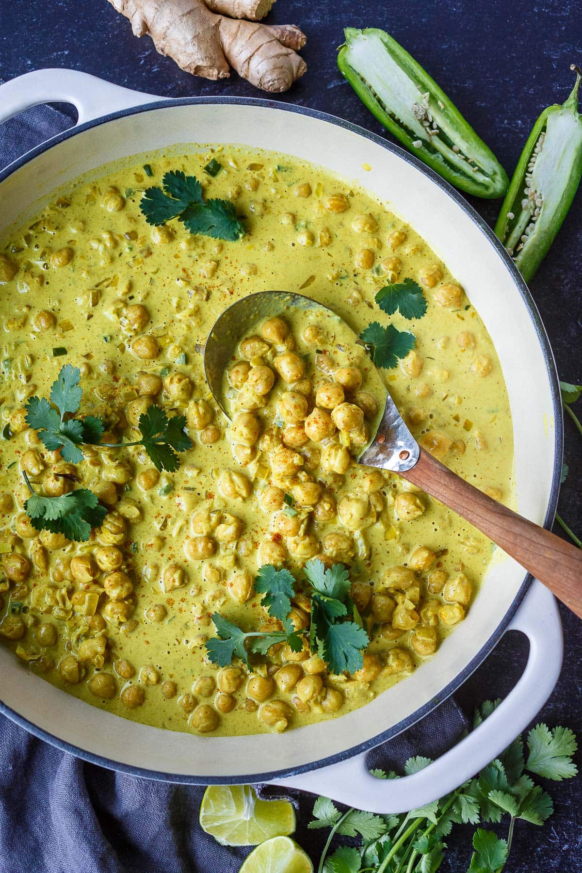 golden chickpea curry in large pan with wood spoon and garnished with cilantro.