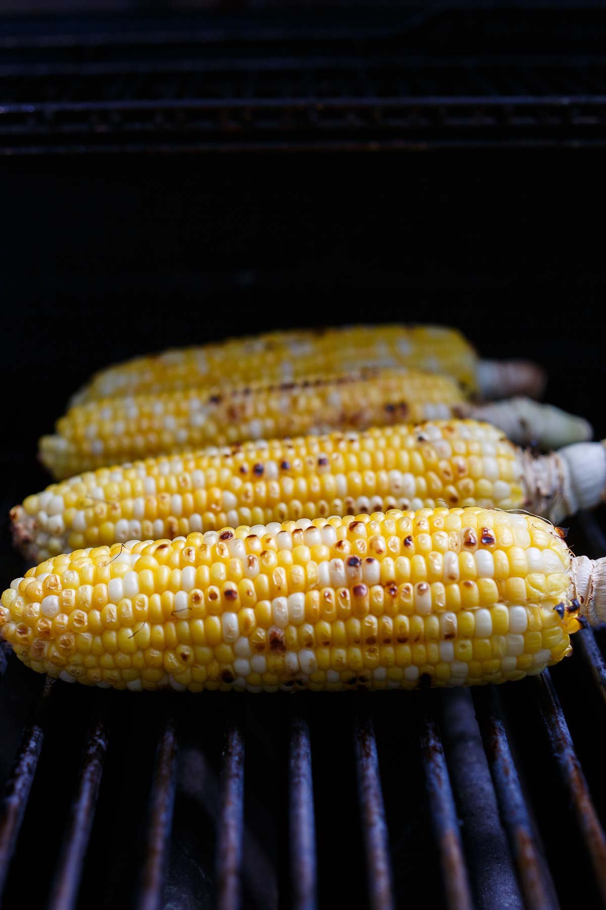 four corn on the cob pieces charring on the grill.