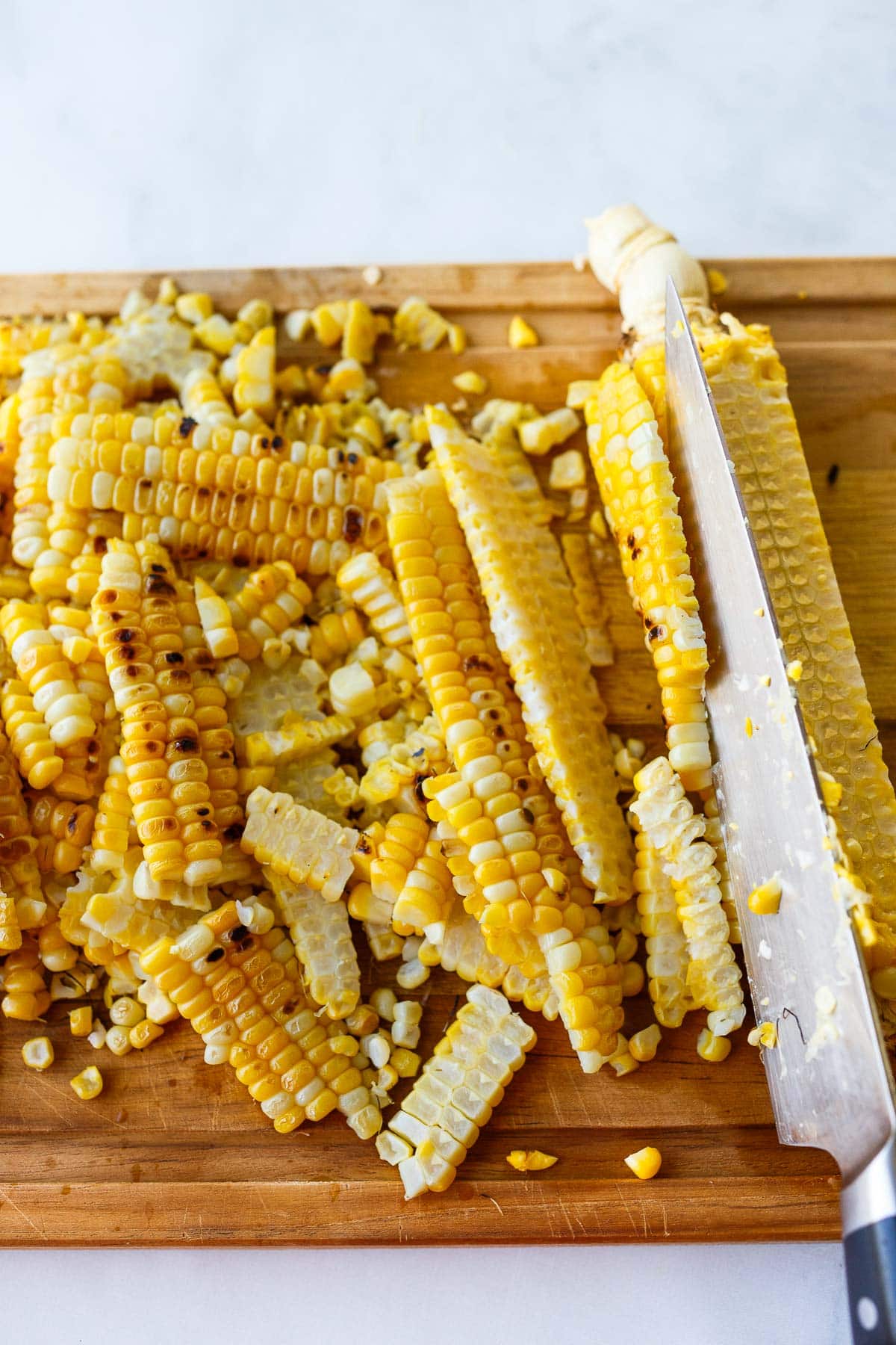 sharp knife cutting corn off the cob on wood cutting board.